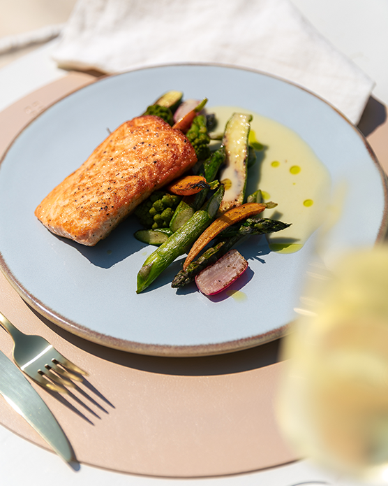 Saumon grillé avec des légumes, servi sur une assiette posée sur une table dressée 