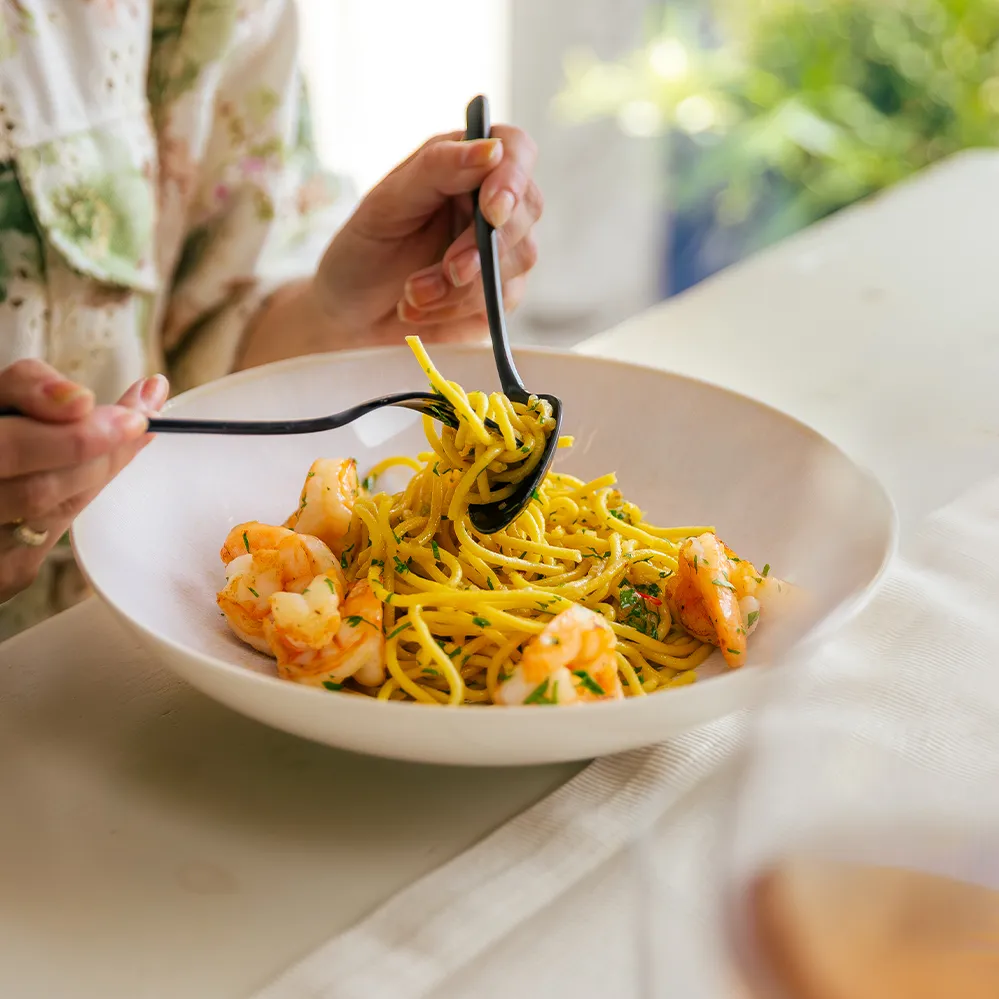 Spaghettis aux crevettes dans un bol beige, servis avec une fourchette et une cuillère