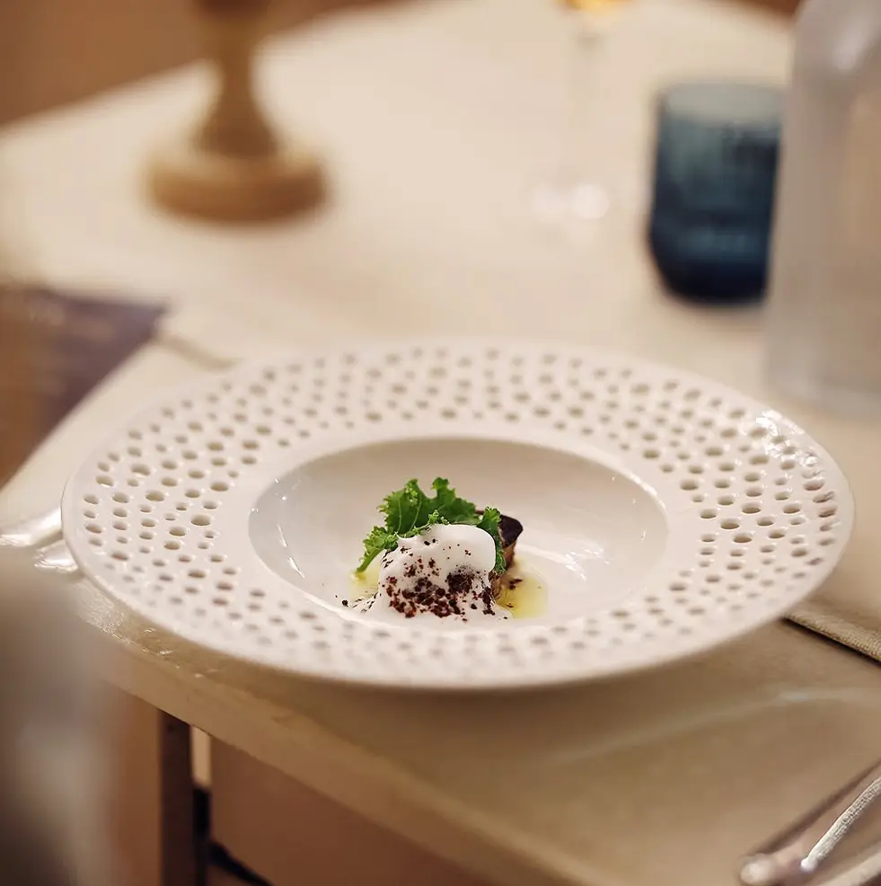 Détail d’un plat servi dans une assiette creuse blanche au bord ajouré